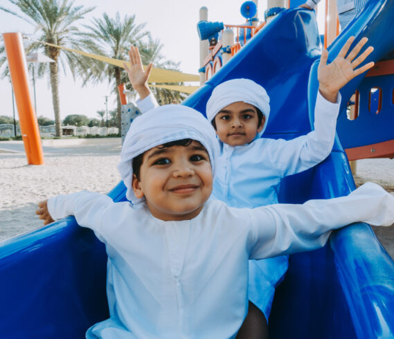 Children playing together in Dubai in the park. Group of kids wearing traditional kandura white dress from arab emirates